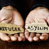 hands hold out pieces of paper with words refugee and asylum