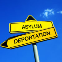 Yellow road signs that read asylum and deportation